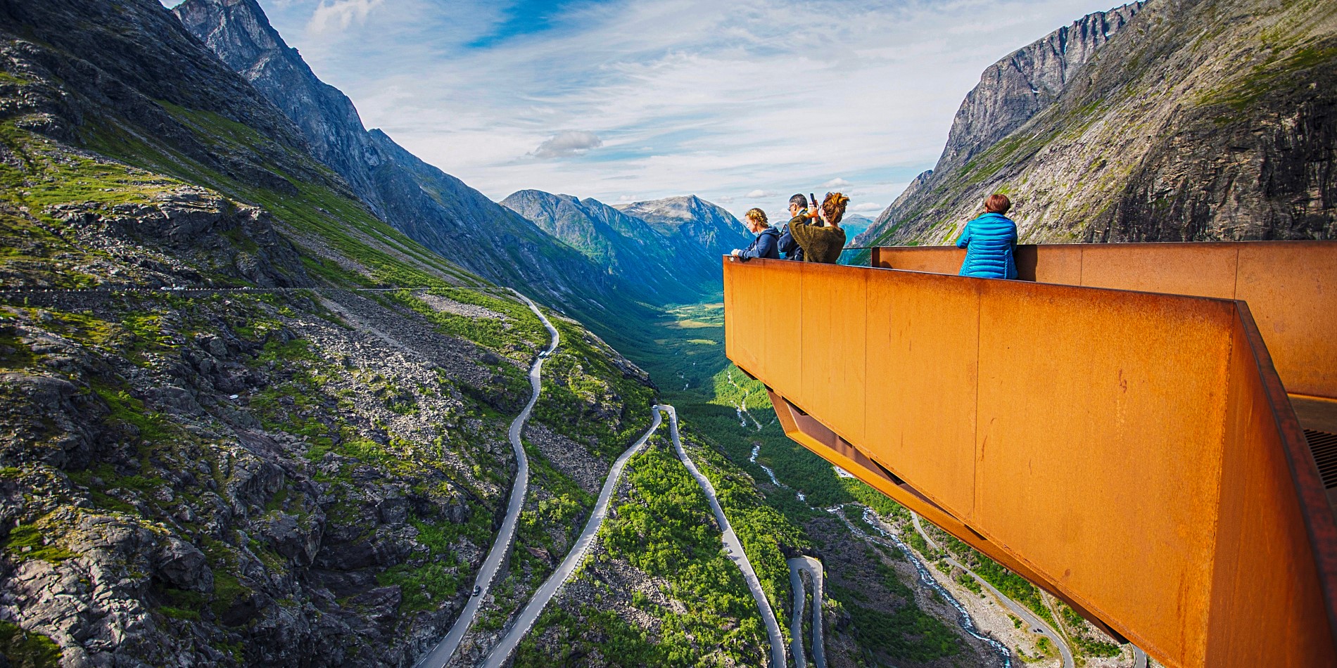 A group of people standing on a view point overlooking Trollstigen