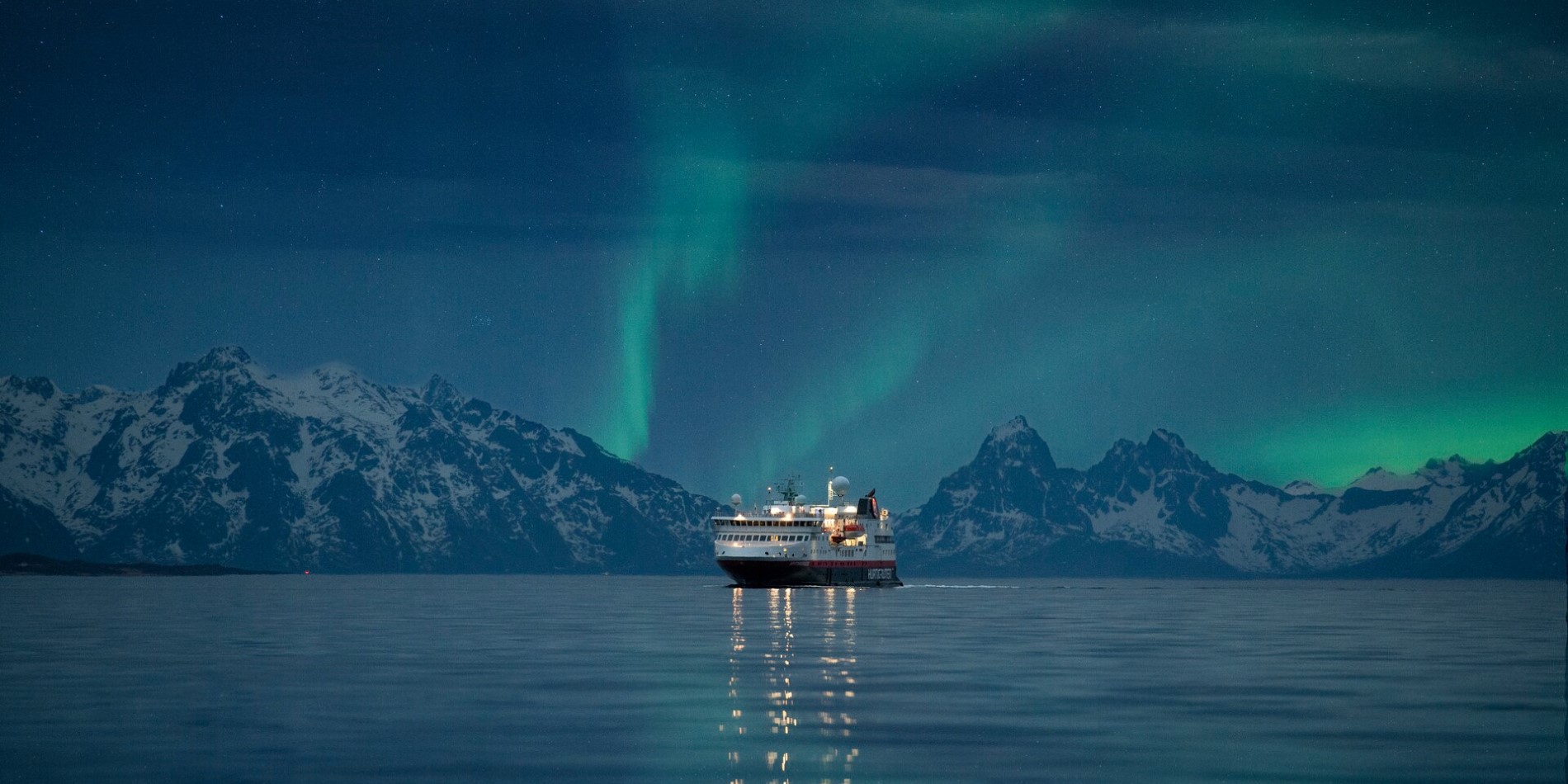 A Hurtigruten ship sailing in Norway with the Northern Lights above